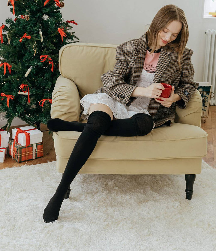Woman sitting on a beige armchair holding a red gift box next to a decorated Christmas tree.