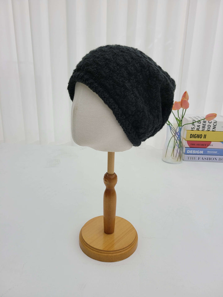 Black knit beanie on a mannequin head with a wooden holder against a white background