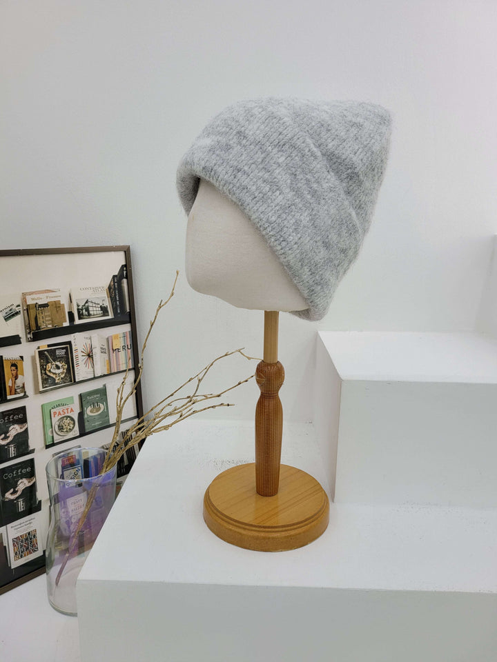 Gray knit hat on a mannequin head with a wooden lamp against a white wall.