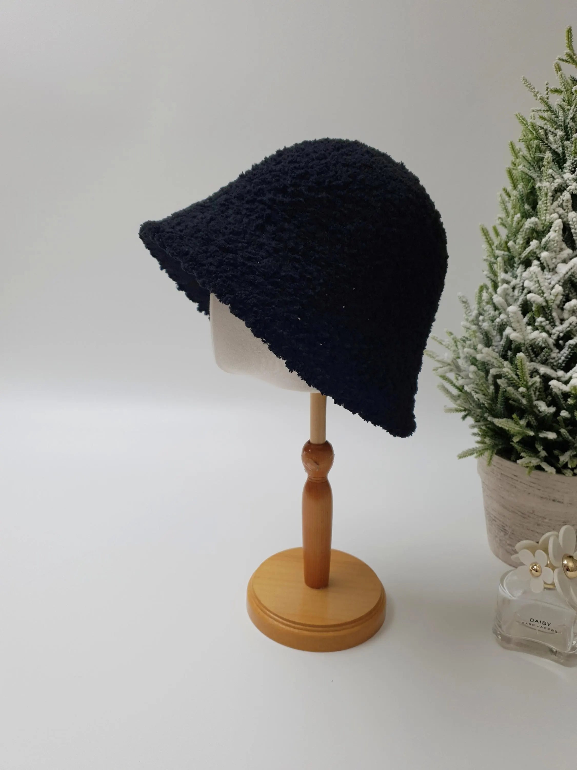 Black sherpa bucket hat on a wooden stand. A cozy and stylish sherpa bucket hat.