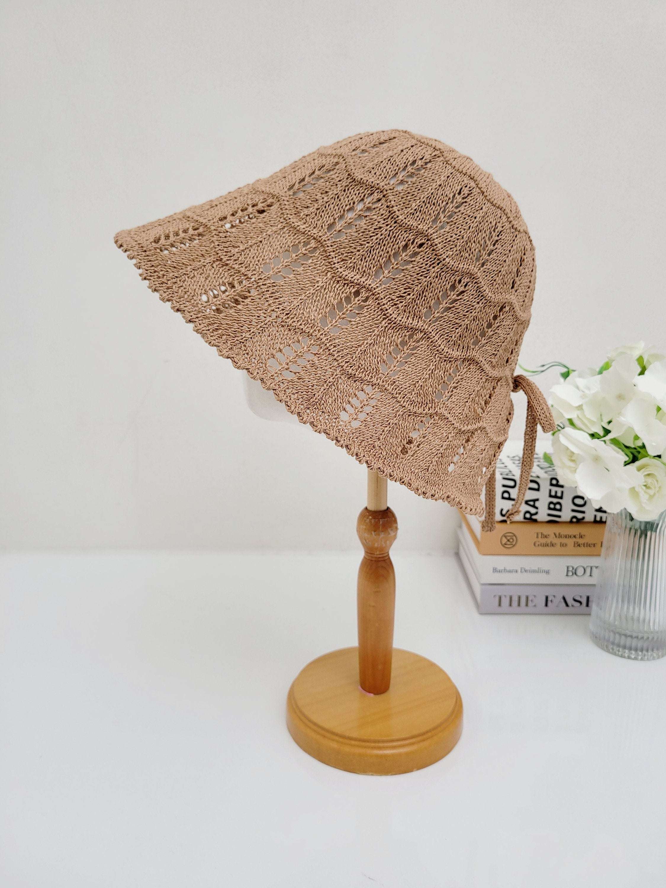 Light brown crocheted sun hat, ashley's summer favorite, with a wavy brim and tie detail, displayed on a wooden stand.