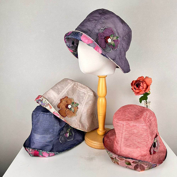 linen bucket-side flower hats in purple, beige, blue, and pink. Each features floral detail and patterned brim. Stylish sun protection.