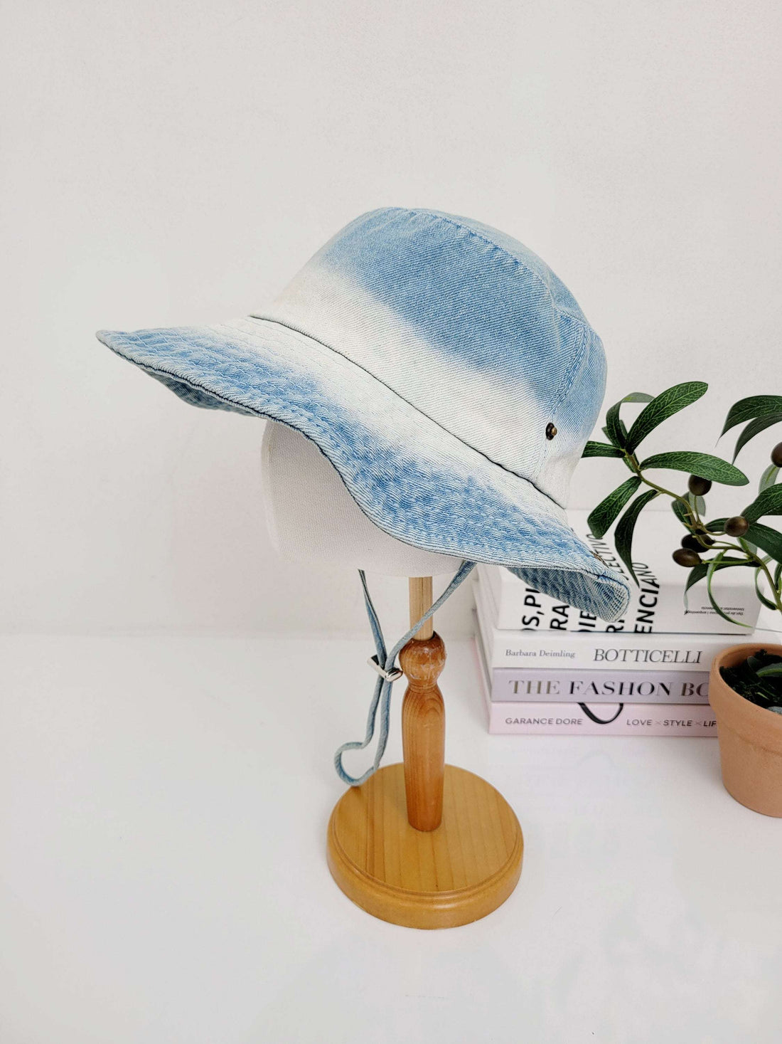 Light blue ombre cotton denim hat with adjustable tie, displayed on a wooden stand.