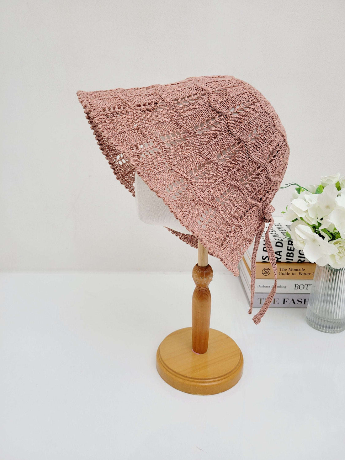 Pink crocheted sun hat, ashley's summer favorite, with a wavy brim and tie strings, displayed on a wooden stand.