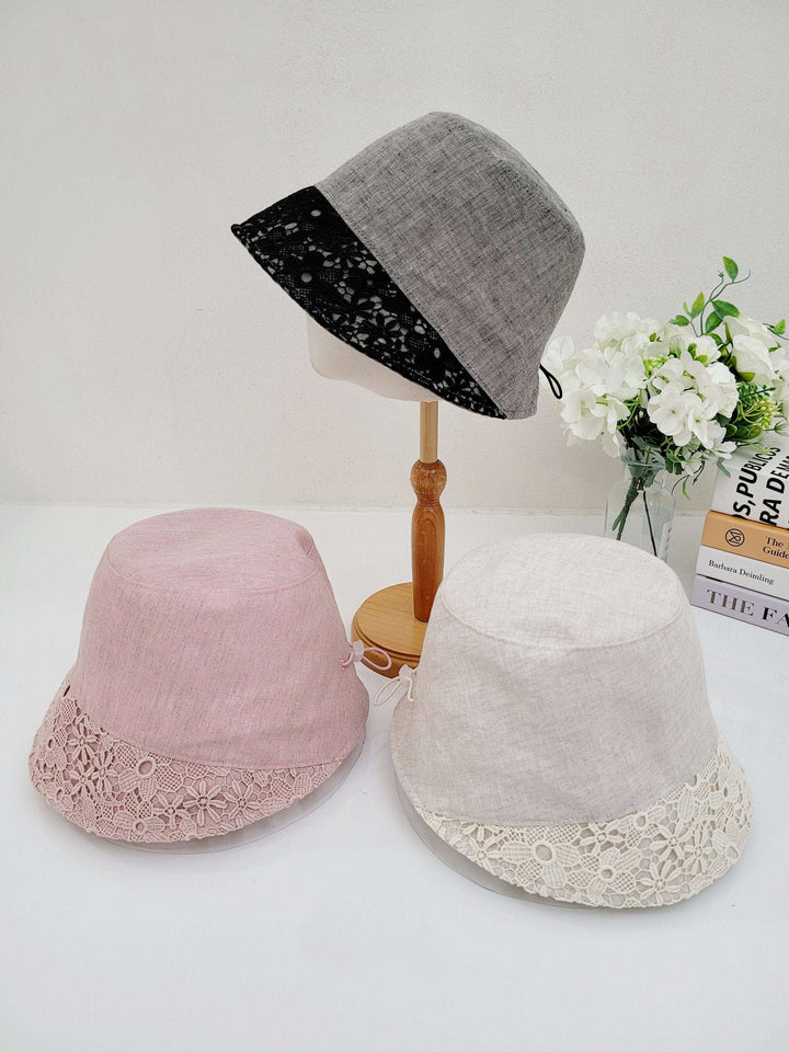 Three linen bucket-flower eyelet hats: gray on a stand, plus pink and cream versions on a white surface, all with delicate lace trim.