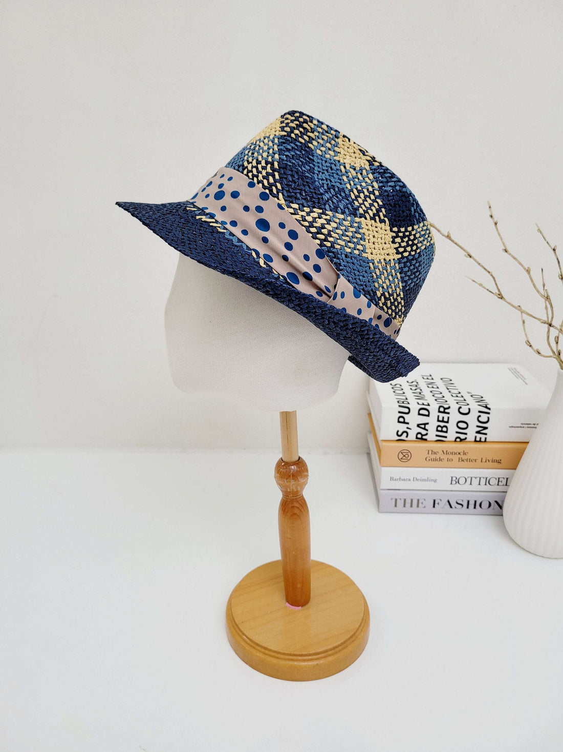 Breezy fedora with a blue and tan woven pattern, accented by a polka dot band. Stylish sun hat displayed on a wooden stand.