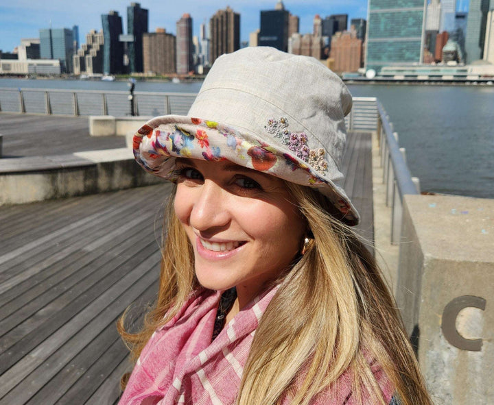 Woman wearing a floral linen bucket-folderable hat with a colorful floral brim, smiling with city skyline in the background.