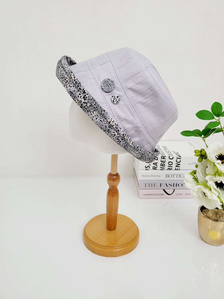 Grey linen bucket hat with a black and white leopard patterned brim and two decorative buttons; a stylish and foldable design. This is the leopard linen bucket-folderable.
