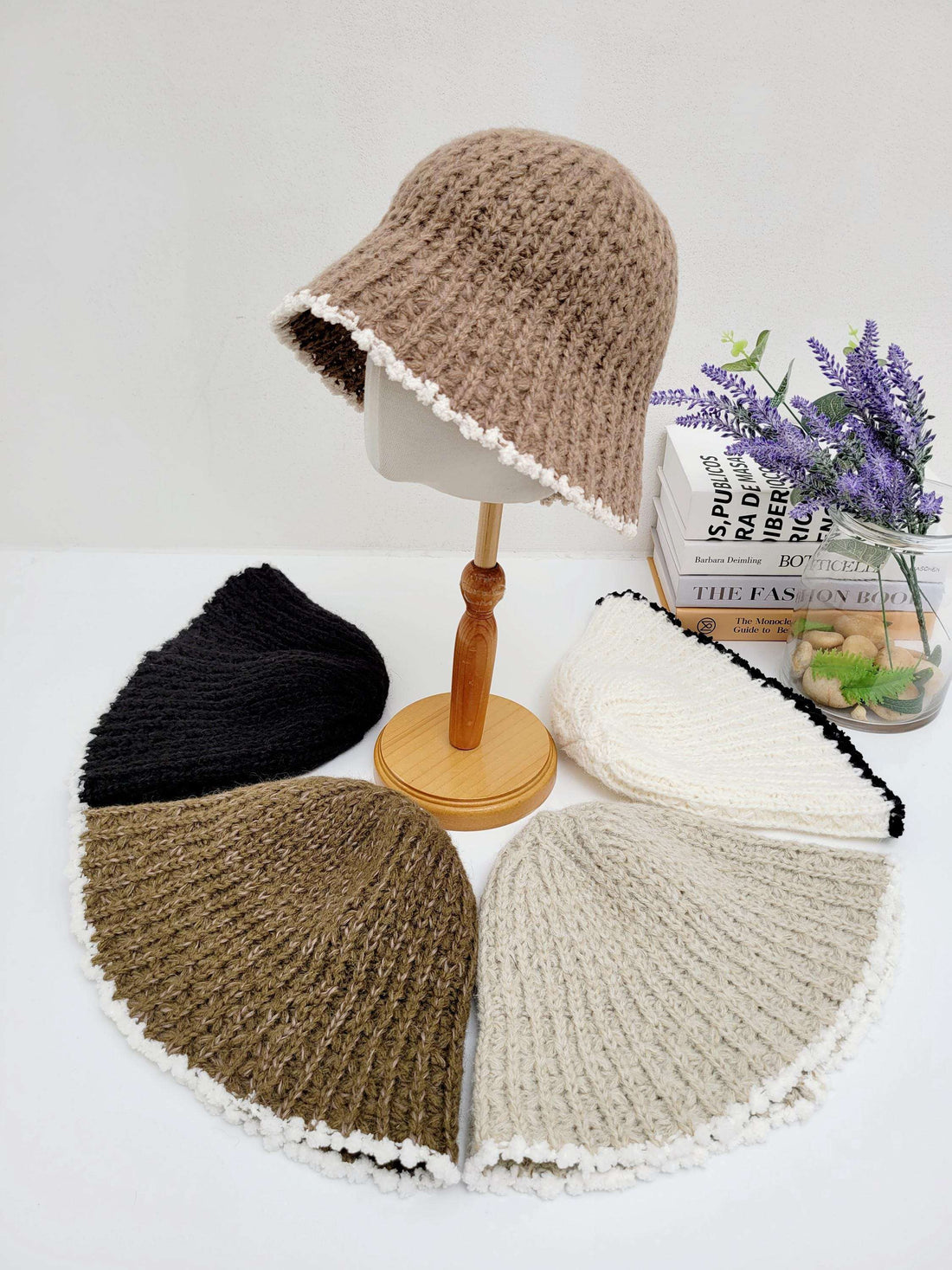 Brown vintage knitted beanie bucket hat on a stand, with white trim. Additional knitted beanies in black, brown, beige, and white are displayed around it.