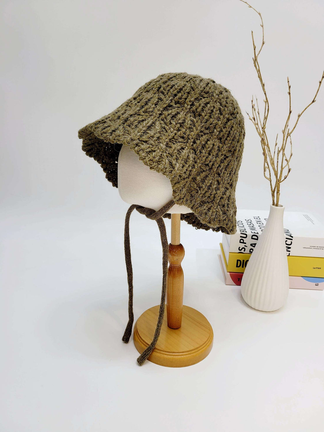 Braided wool hat in olive green, a cozy knitted bucket hat with tie strings displayed on a mannequin head.