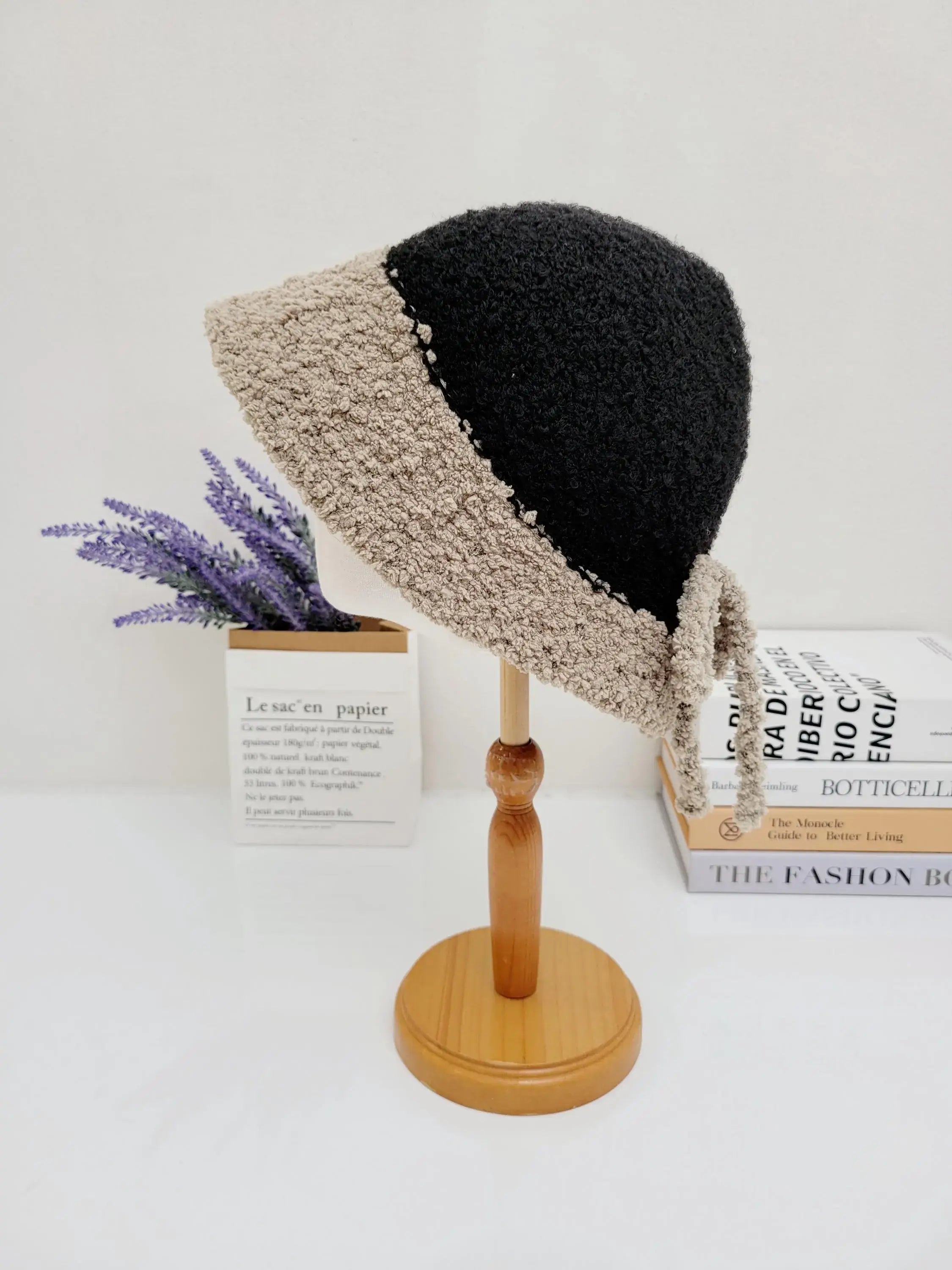 Black and beige sherpa boho bucket hat on a wooden stand. Cozy textured fabric with tie detail, perfect for a stylish, warm look.