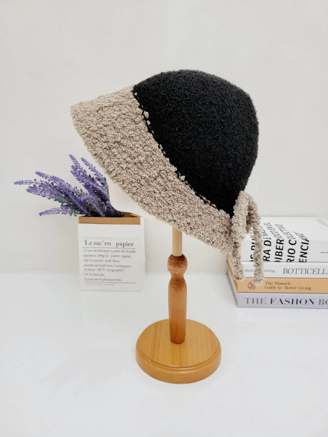 Black and beige sherpa boho bucket hat on a wooden stand. Cozy textured fabric with tie detail, perfect for a stylish, warm look.