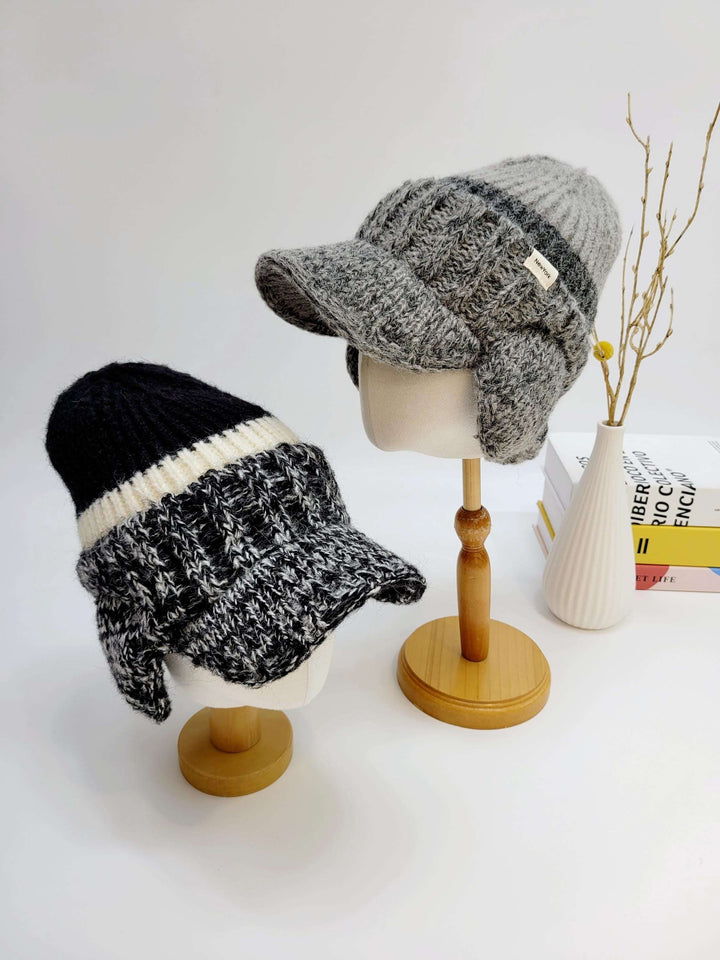 Two knit brooklyn trapper hats: one in gray with ear flaps, the other in black and white, both with brims.