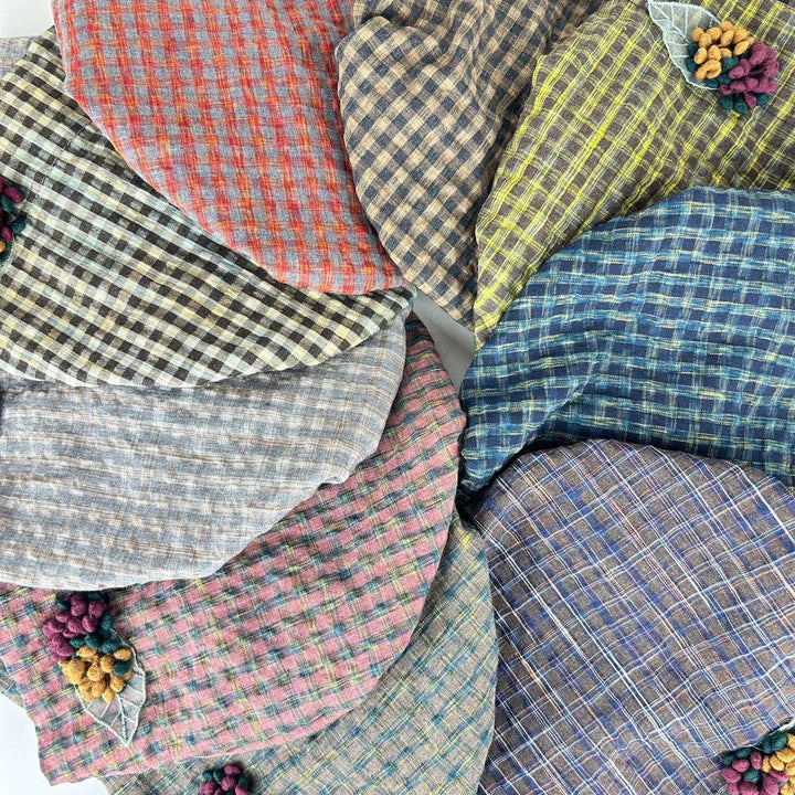 Assorted checkered beanie hats in colors like red, blue, yellow, and brown, arranged in a circle. Each chekered beanie features a small floral accent.