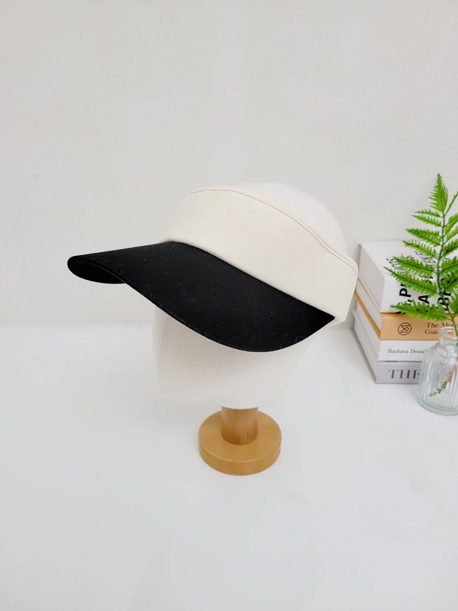 sports sun visor with a white top and black brim, displayed on a mannequin head atop a wooden stand