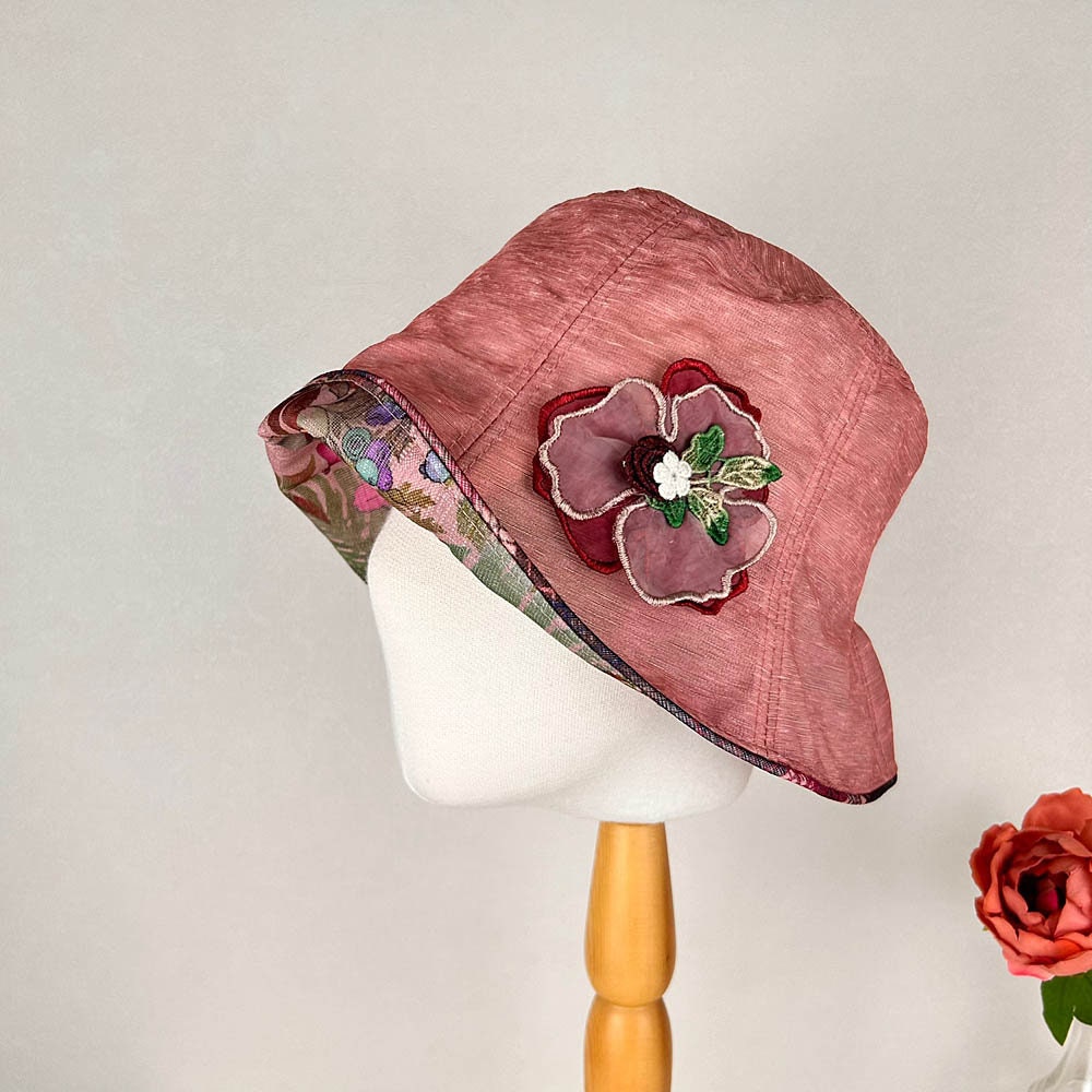 Pink linen bucket-side flower hat with floral brim detail and a decorative flower accent. Stylish sun protection.