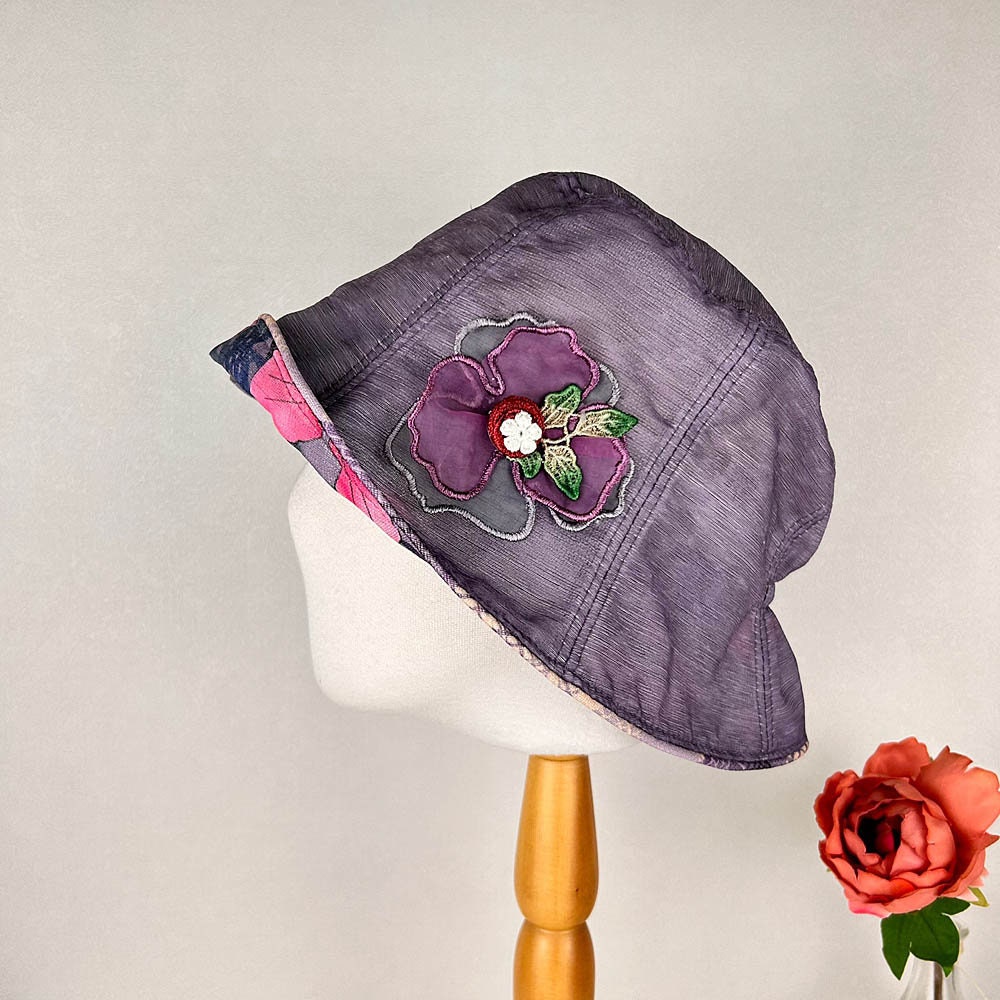 Purple linen bucket-side flower hat with floral applique. A stylish, sun-protective accessory.