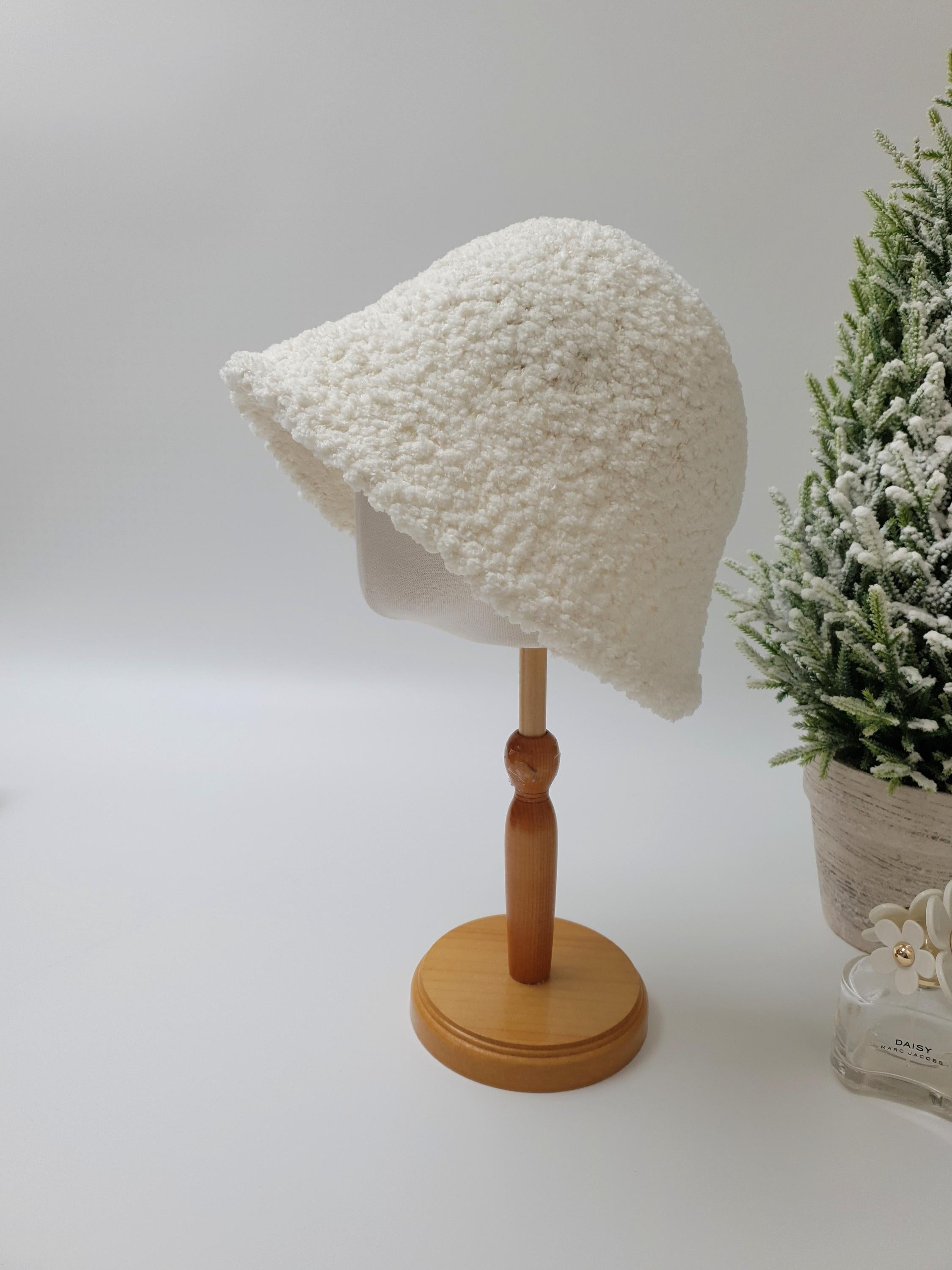 Soft, textured white sherpa bucket hat displayed on a stand, offering cozy warmth and casual style