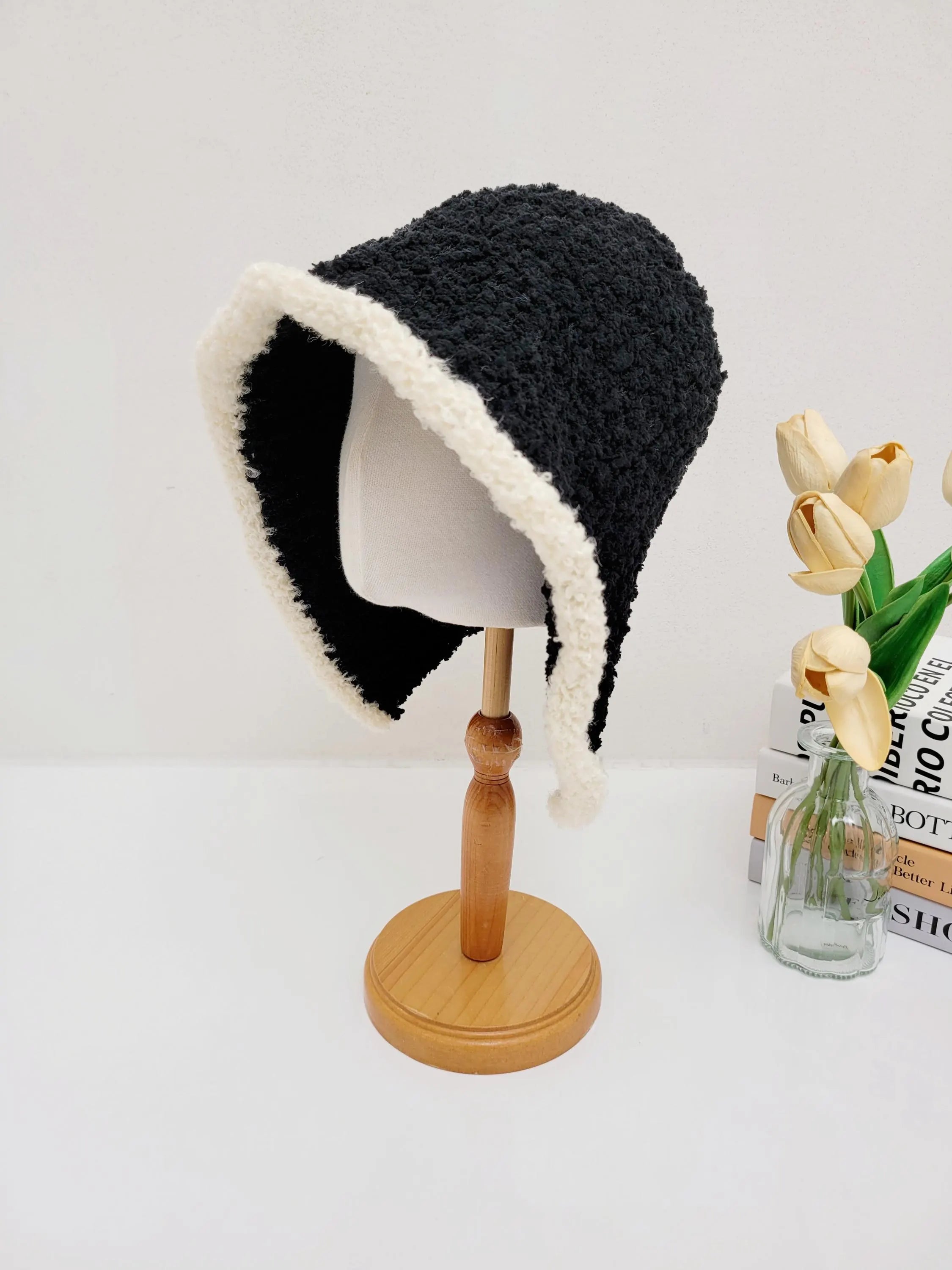 Black wool hooded hat with soft white trim, displayed on a wooden stand. Cozy and stylish.