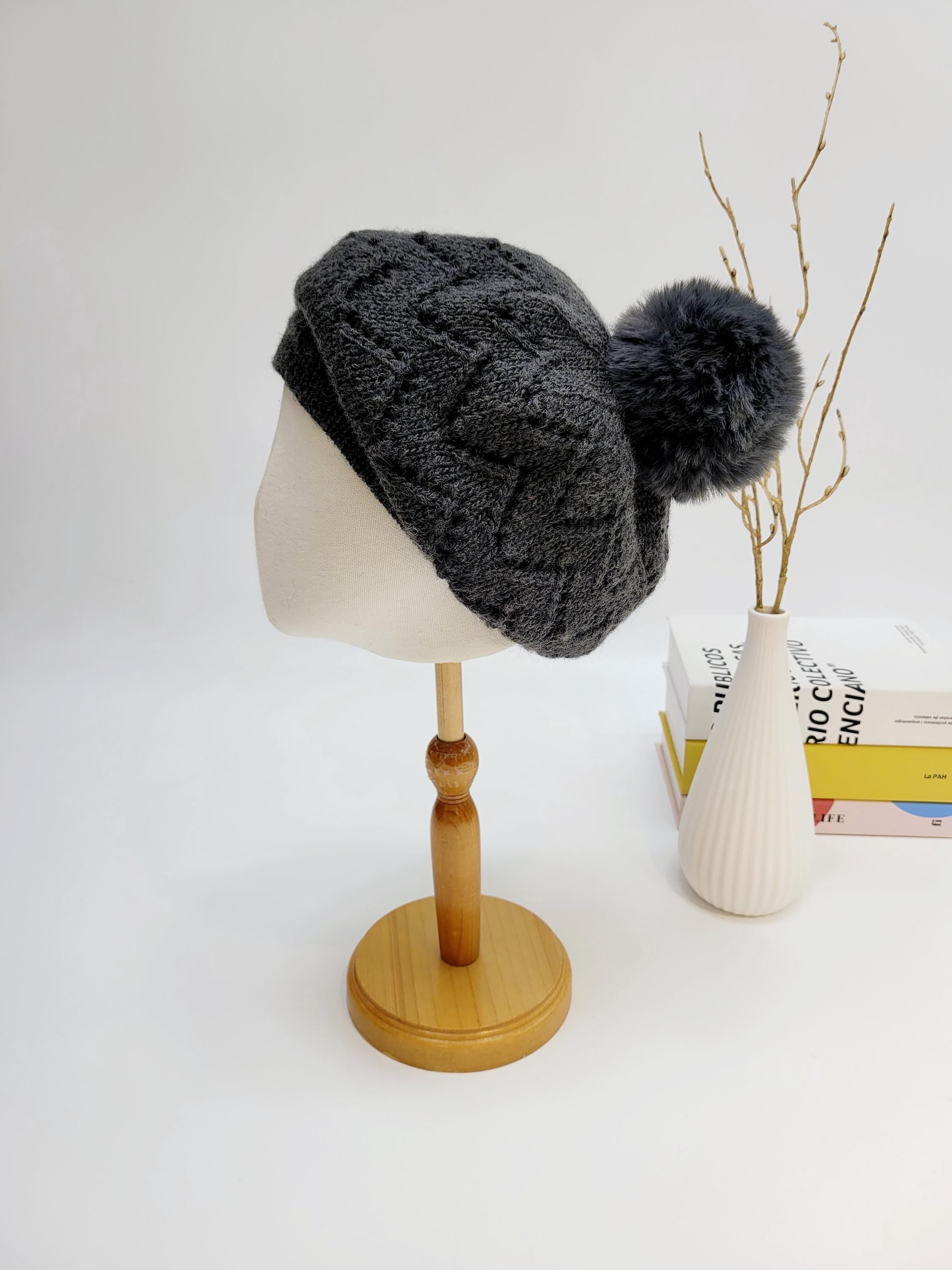 Dark gray knitted emma in paris beret with a fluffy pompom, displayed on a mannequin head. Stylish and cozy headwear.