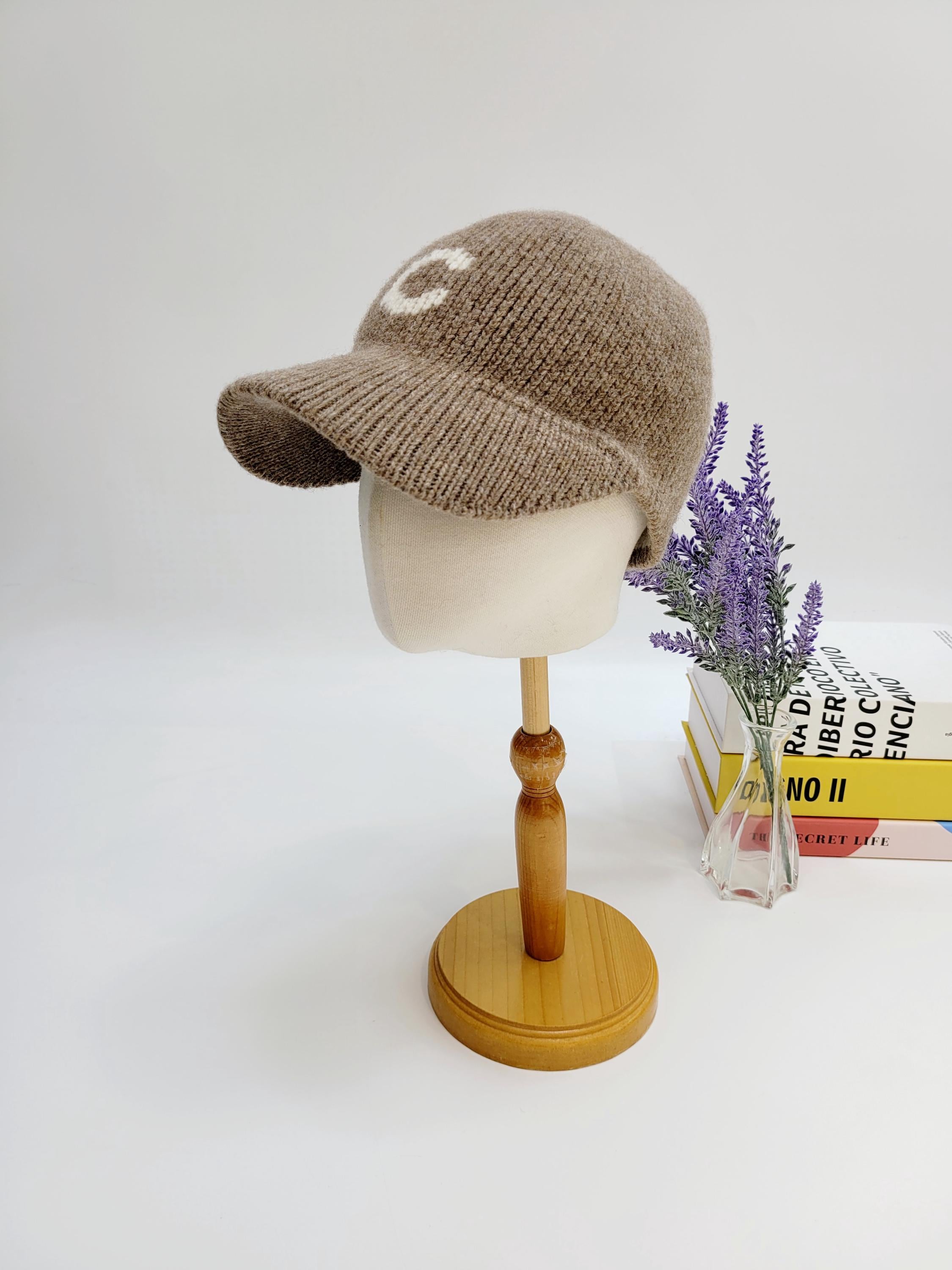 Beige knitted c-wool cap with short brim and white "C" detail on the front, displayed on a mannequin head.
