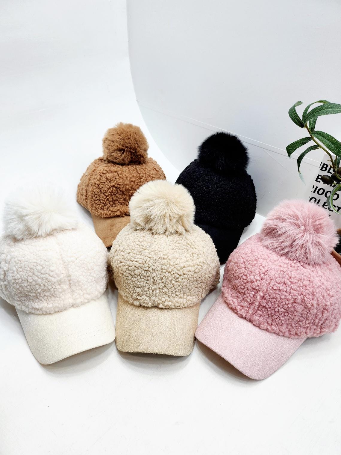 Soft adriana sherpa cap in cream, tan, beige, black, and pink. Each cozy hat features a matching pompom and brim.