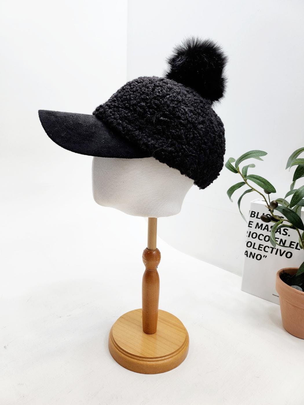 Black adriana sherpa cap with suede brim and pompom, displayed on a mannequin head