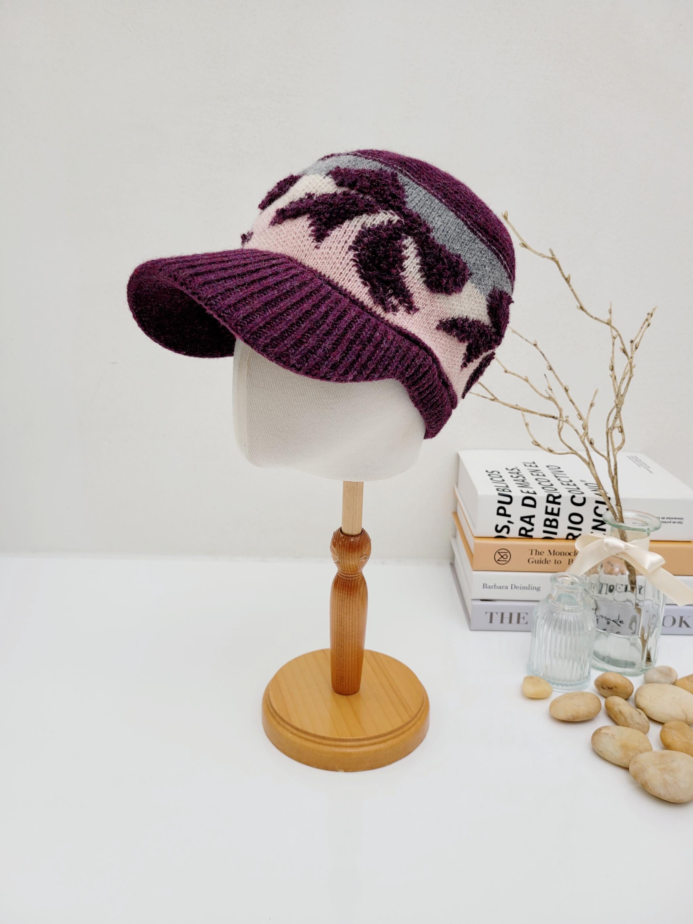 EARMUFF knitted wool cap: Stylish purple knit cap with a short brim and stylized leaf pattern in white, pink, and gray.